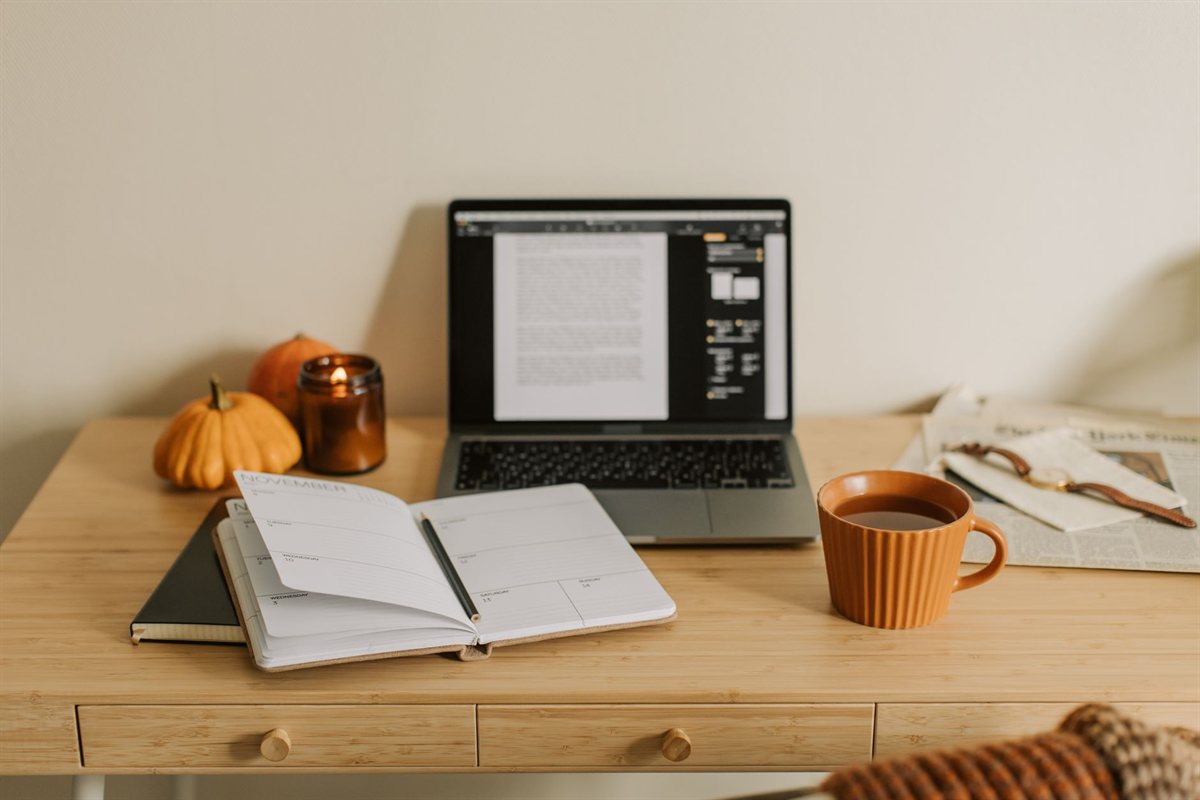 Agenda semanal aberta ao lado de laptop, vela acesa e café.